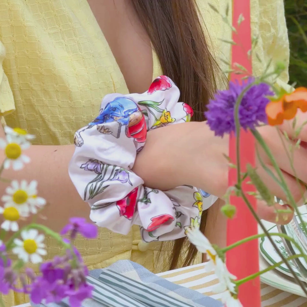 Video of a summer tablescape featuring a girl fixing a floral paddington scrunchie in the garden