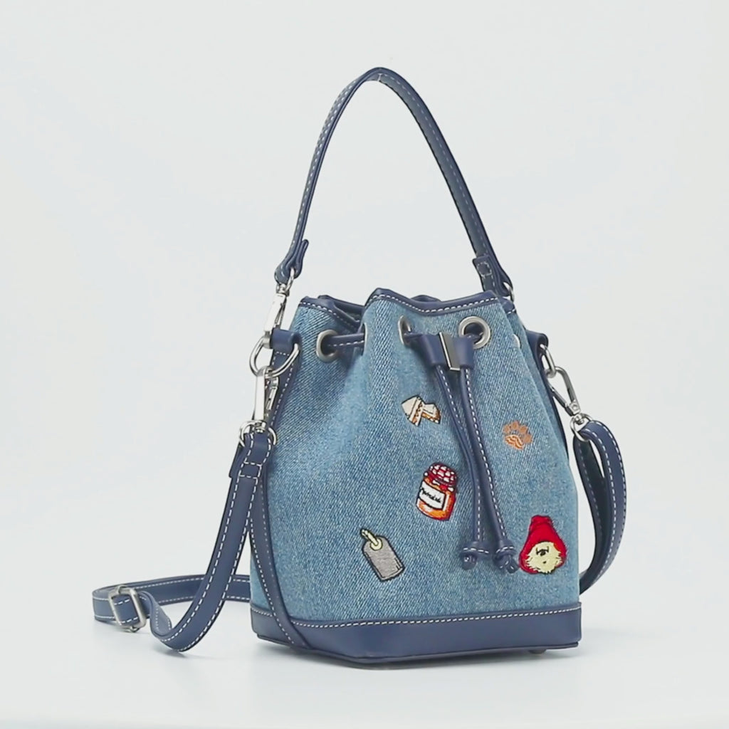 Paddington P.B. Collection denim bucket bag with adjustable strap, drawstring-style shape and Paddington detailing shown in close-up.