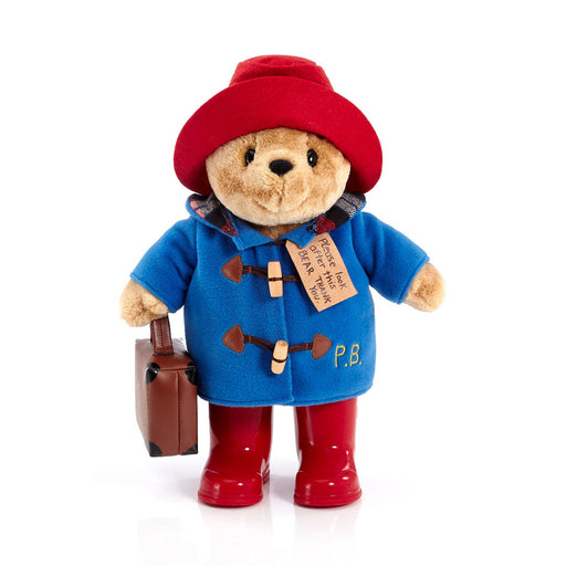 A plush toy of Paddington Bear wearing a blue duffle coat, red hat, and red boots, holding a suitcase.