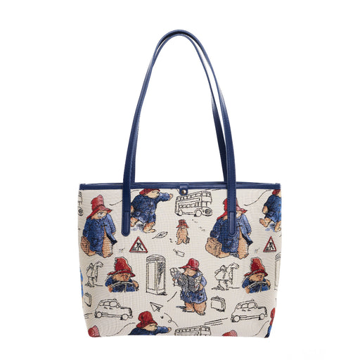 A beige tote bag featuring a tapestry design with characters and a cityscape, accented with faux leather trim and blue handles.