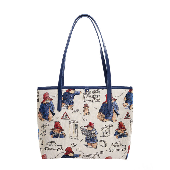 A beige tote bag featuring a tapestry design with characters and a cityscape, accented with faux leather trim and blue handles.