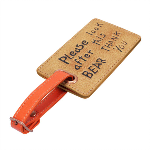 A beige luggage tag with 'Please look after this BEAR THANK YOU' written on it, featuring an orange buckle closure and a flap for contact details.